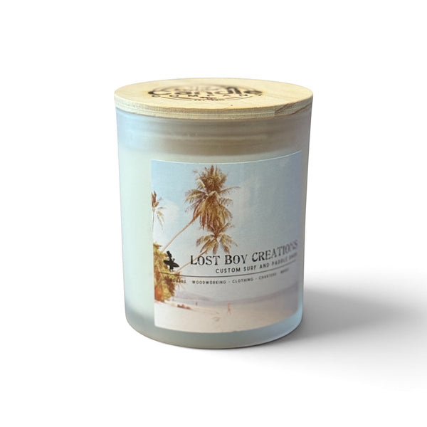 Lost Boy Signature Candle — front view, LBC logo and palm trees on beach glass jar with off-white wax and wood lid | Lost Boy Creations Key West