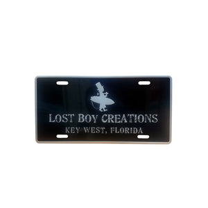Black license plate with 'Lost Boy Creations Key West, Florida' text and silhouette on a white background