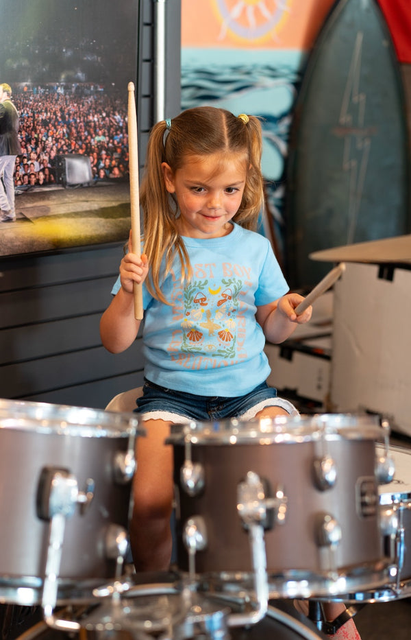 Girl wearing Kid's Day Trippin Tee in Sky Blue playing drums in the Lost Boy Creations shop | Lost Boy Creations Key West