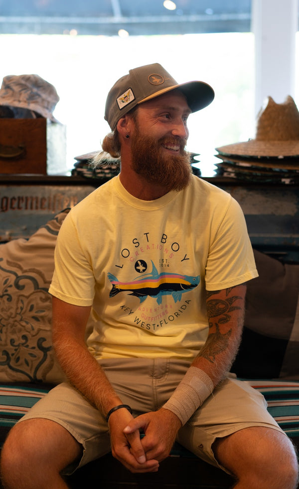 Men's Silver King Tee — lifestyle, man wearing Silver King Tee seated in Lost Boy Creations store with hats displayed in background | Lost Boy Creations Key West