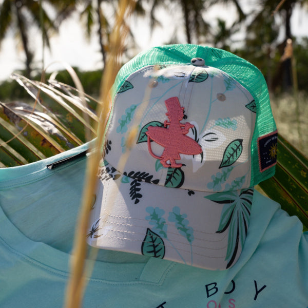 Coral Cruiser beige floral low crown trucker hat staged outdoor display with palm trees in the background | Lost Boy Creations Key West