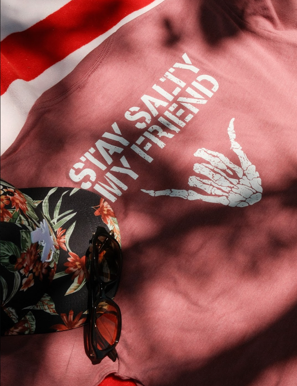 Stay Salty Shaka 2.0 Tee in Mauve — graphic back lifestyle flat lay, white 'Stay Salty My Friend' text with skeleton shaka hand graphic | Lost Boy Creations Key West