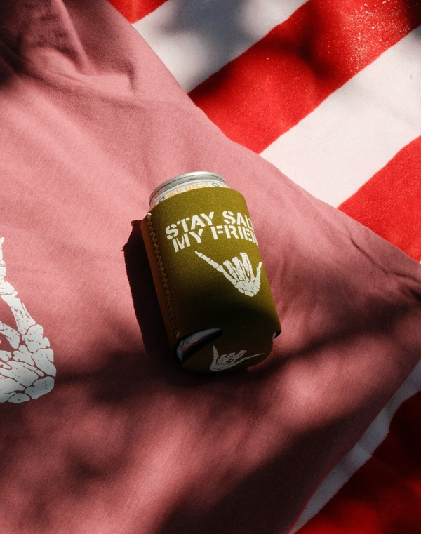 Lost Boy Koozie - Stay Salty in Olive — lifestyle shot, white Stay Salty My Friend skeleton shaka graphic, red and white towel background | Lost Boy Creations Key West