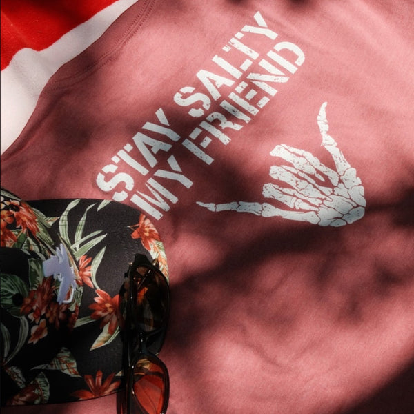 Stay Salty Shaka 2.0 Tee in Mauve — graphic back lifestyle flat lay, white 'Stay Salty My Friend' text with skeleton shaka hand graphic | Lost Boy Creations Key West