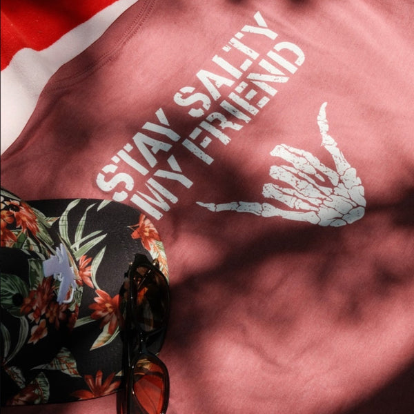 Stay Salty Shaka 2.0 Tee in Mauve — graphic back lifestyle flat lay, white 'Stay Salty My Friend' text with skeleton shaka hand graphic | Lost Boy Creations Key West