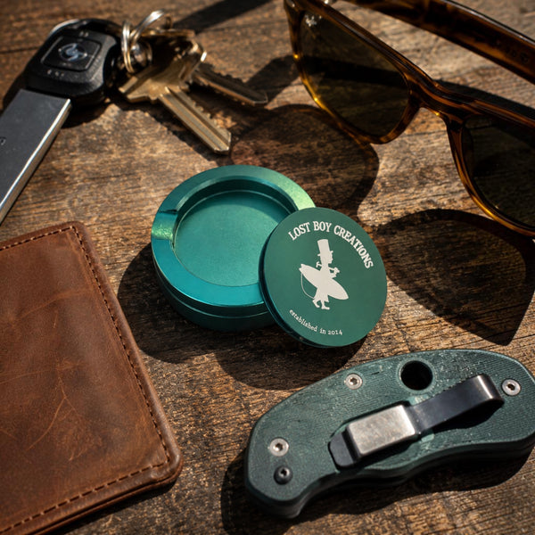 Utility Pocket Tin in Dark Green — lifestyle EDC flat lay, open tin with LBC logo alongside wallet, keys, sunglasses, and pocket knife | Lost Boy Creations Key West