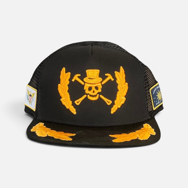 A Pirate's Life for Me Hat in Black — front flat, yellow pirate skull & crossbones emblem, gold laurel wreath on front panels & brim, black mesh back | Lost Boy Creations Key West