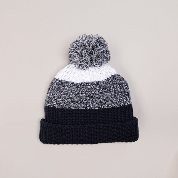 Lost Boy Creations chunky knit pom pom beanie in navy, grey, and white with a fold-over cuff.