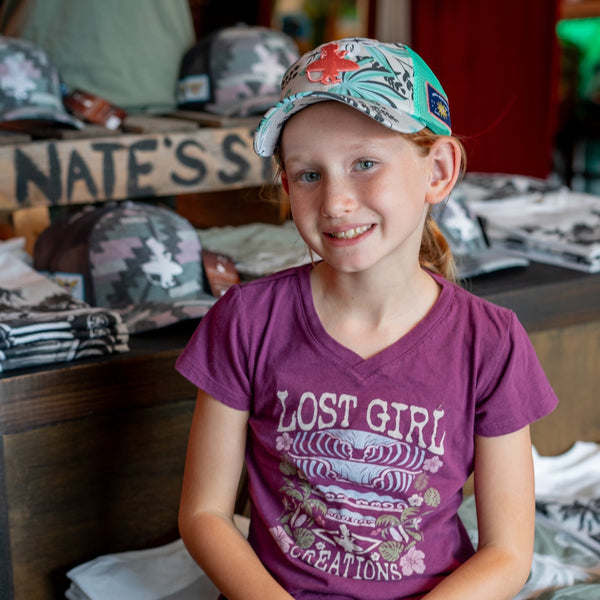 Kid's Tahiti Tee dragonfruit lifestyle shot worn by girl in Lost Boy Creations shop with Lost Girl surf graphic | Lost Boy Creations Key West