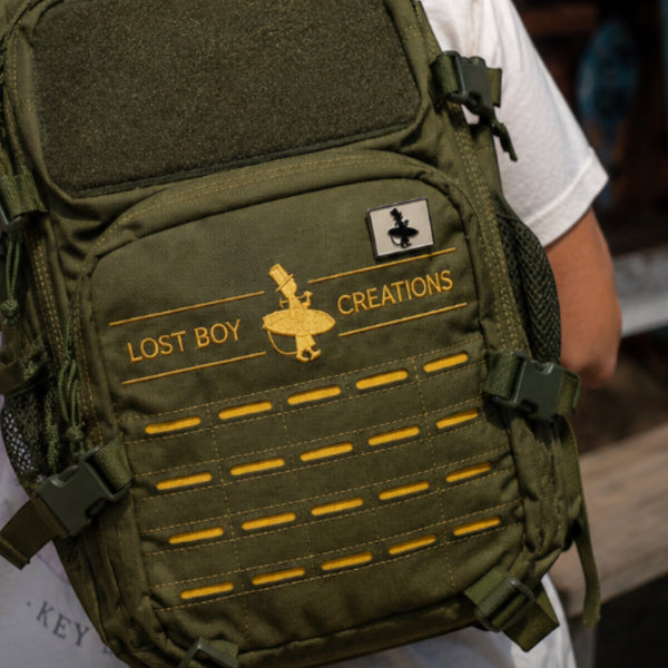LBC Collectible Pin white and black enamel lifestyle shot pinned to olive green tactical backpack with Lost Boy Creations embroidery | Lost Boy Creations Key West