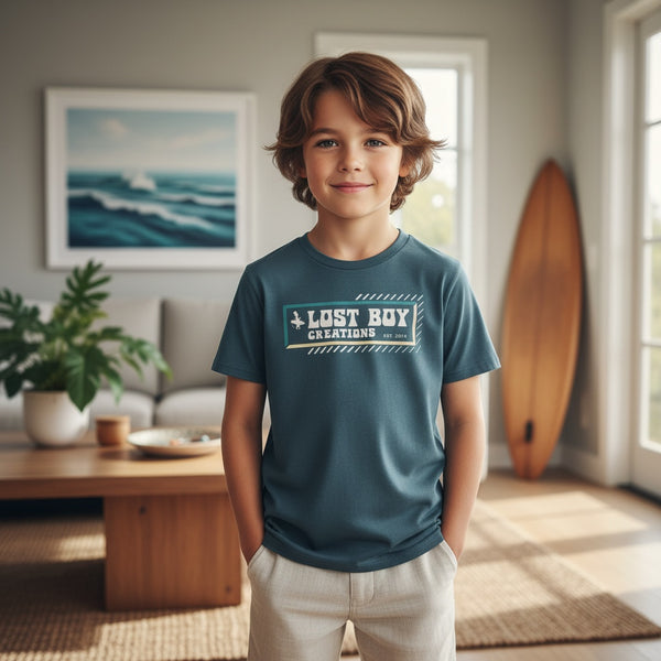Kid's Lost Boy Explorer Tee indigo lifestyle shot worn by boy in coastal living room with surfboard in background | Lost Boy Creations Key West