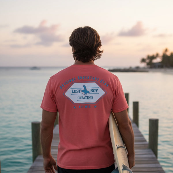 Men's Original Adventure Gear Tee in Nantucket Red — lifestyle, man wearing tee with Original Adventure Gear back graphic on a wooden pier | Lost Boy Creations Key West