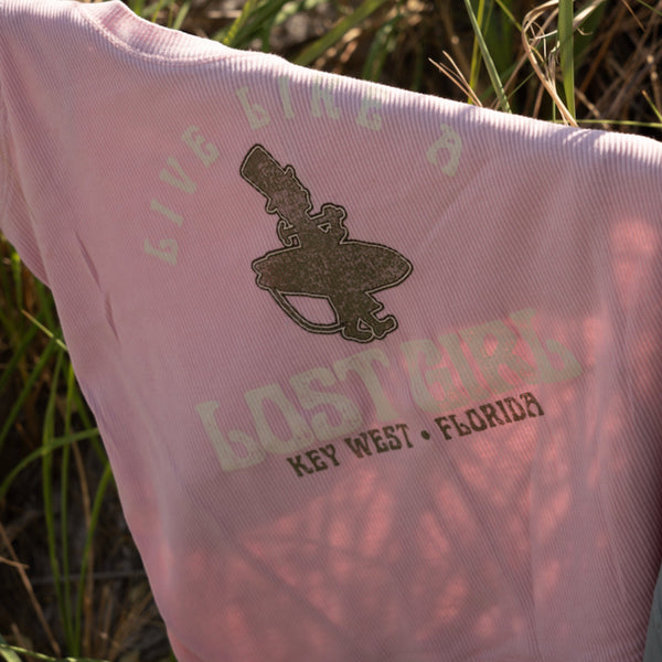 Lost Boy Creations Women's Lost Girl Ribbed Tank in pink held up outdoors showing close-up of Live Like a Lost Girl surfer graphic with Key West Florida text | Lost Boy Creations Key West